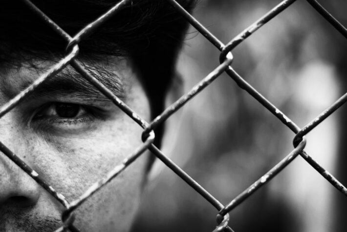 Depressed man standing behind a fence ,close up on face