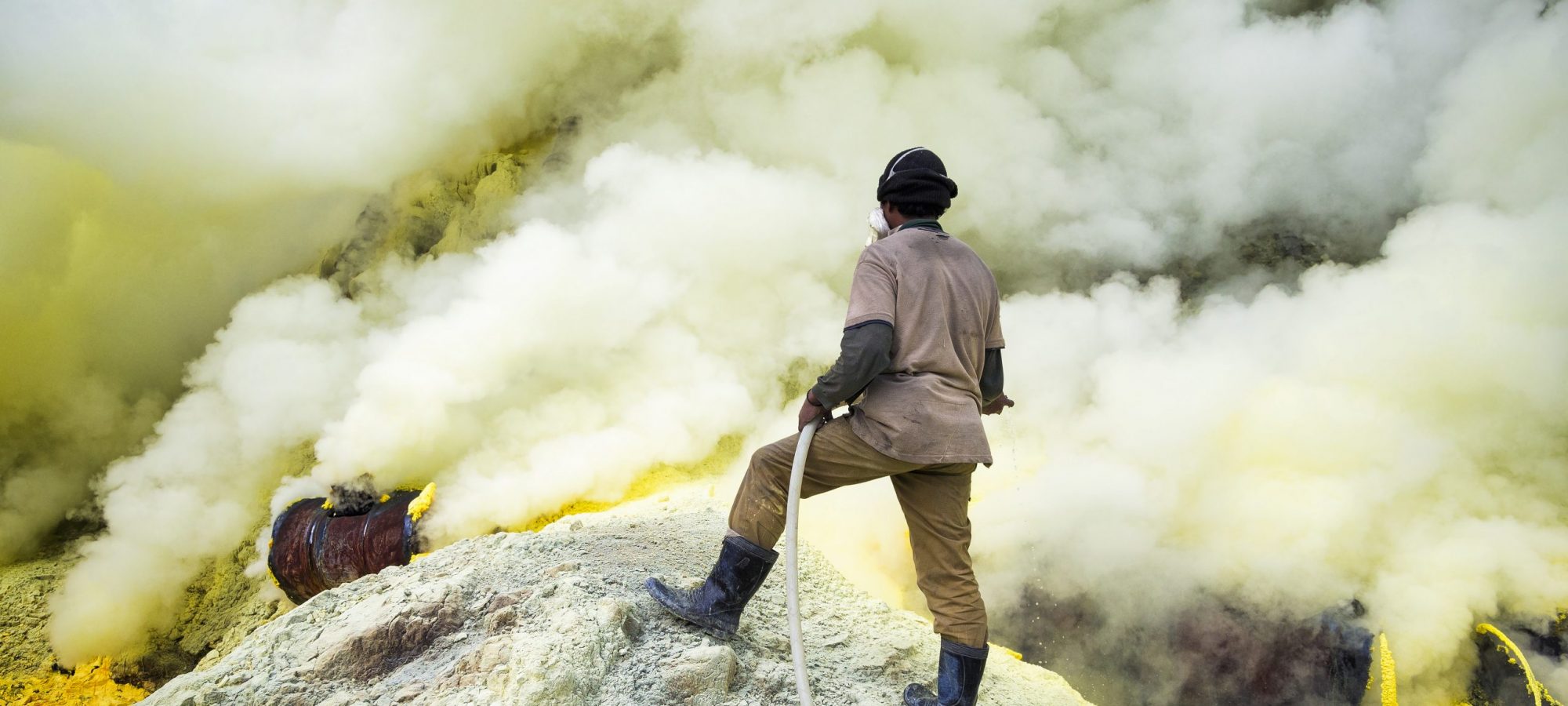 Kawah Ijen Volcano, East Java, Indonesia - May 25, 2013: Sulfur miner spraying water onto pipes inside the crater of Kawah Ijen volcano in East Java, Indonesia..