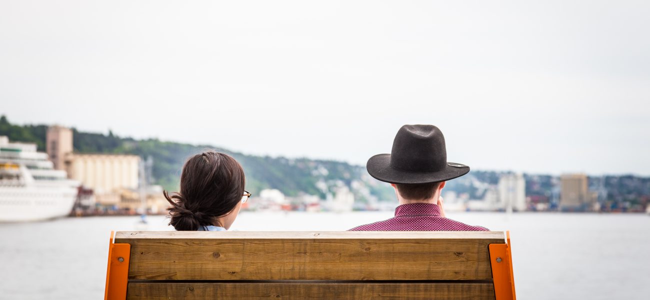 Young couple looking at view on bench in Oslo, Norway. Rear view from behind the bench, while the couple are looking at the Oslo Fjord and harbour in front of them. Horizontal colour image with copy space.