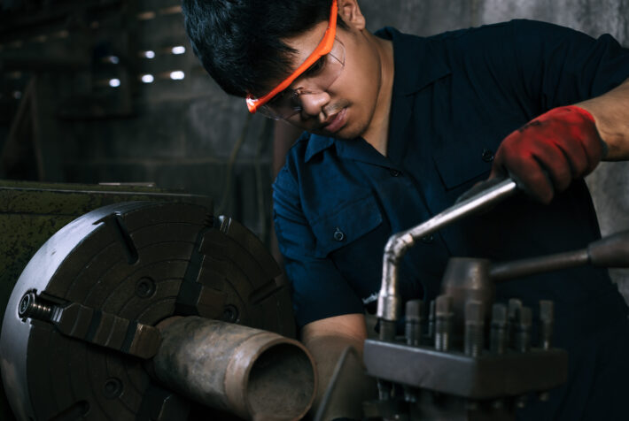 Diverse Asian manufacturing engineer using a socket hand tool to adjust industrial lathe equipment in factory workshop