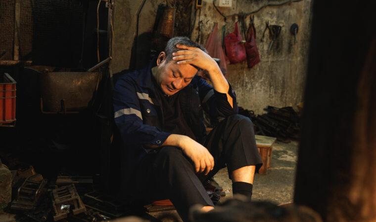 Stressed senior factory worker suffering from headache or fatigue.