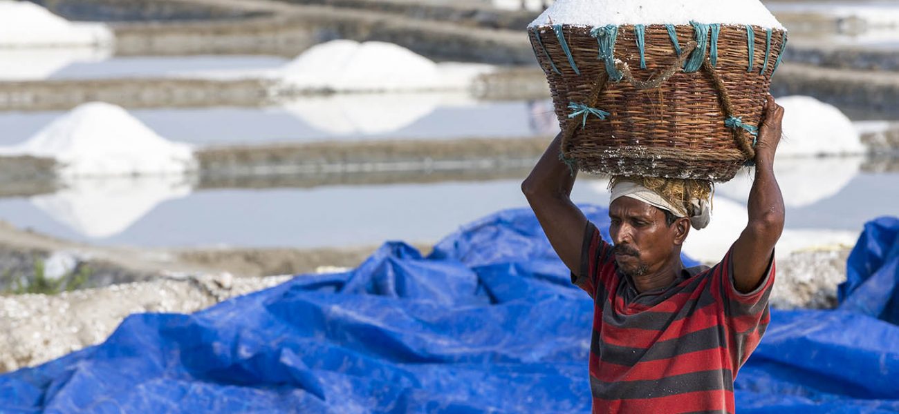 PONDICHERY, PUDUCHERRY, TAMIL NADU, INDIA - MARCH CIRCA, 2018. Unidentified worker carrying wooden baskets full of salt on the head and walking on salt field to the store.